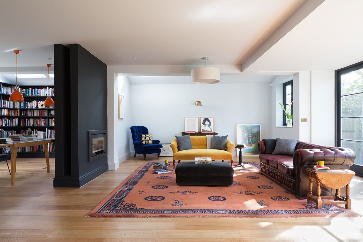 open-plan living room and library with dividing fireplace and oak floor vintage Chesterfield and coloured velvet seating