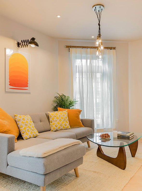 airy modern flat living room with grey felt Howard Swoon Sofa and various orange cushions by Noguchi table and vintage lights