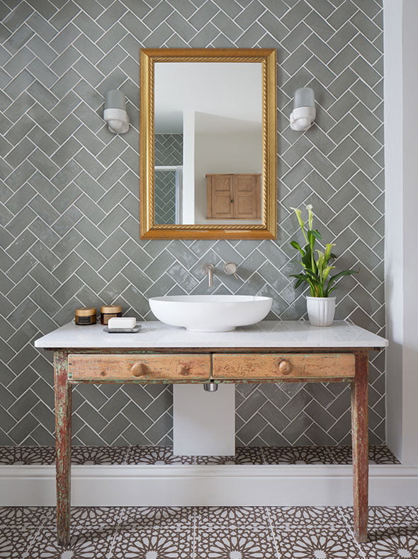 eclectic design of bathroom with sage herringbone tiles and Thomas Hoof porcelain wall lights from SCP behind reclaimed desk