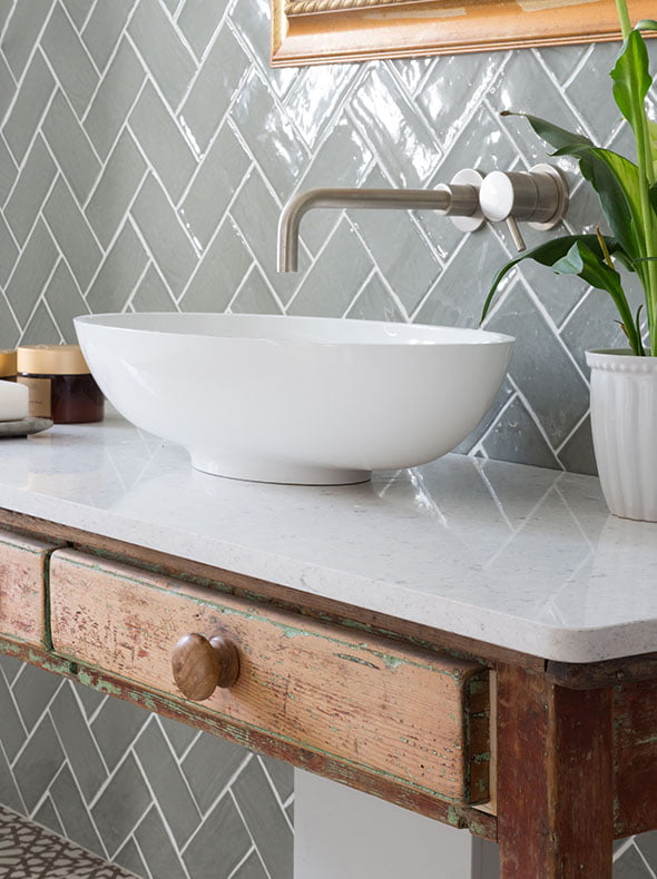 bathroom design by Element Studios showing close-up of vintage wash stand with stone worktop and sage herringbone wall tiles