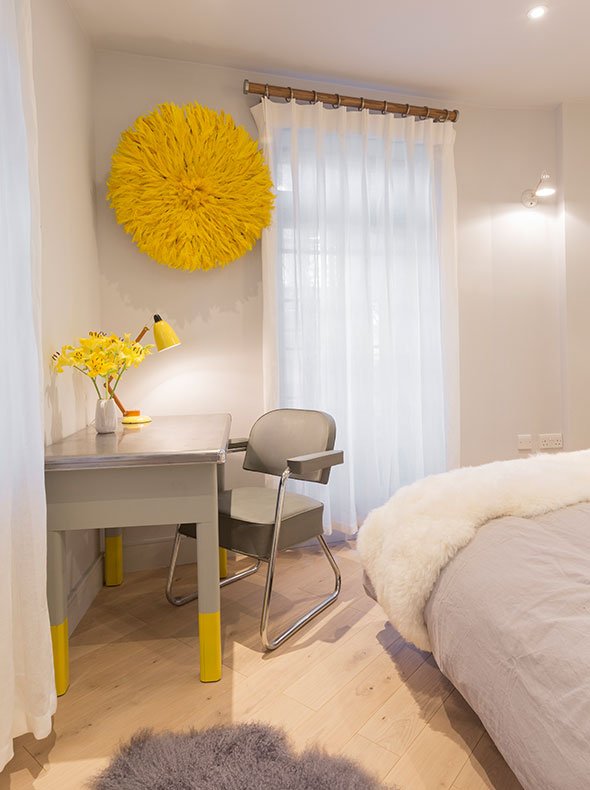 contemporary bedroom interior showing 1950s French writing desk with grey tub chair and Juju yellow hat on wall behind